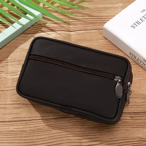 Slim dark brown leather belt waist bag with dual zipper compartments on wood surface