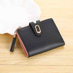 Detail of a minimalist black and pink bifold wallet with gold metal buckle and tassel charm
