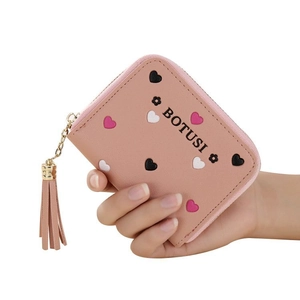 Petit portefeuille rose avec motif cœur, fermeture éclair et pompon tenu à la main