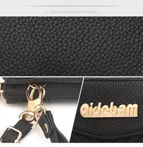 Detail of black pebbled leather texture with gold-tone hardware hooks and metal logo