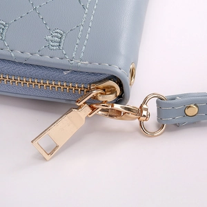 Detail of light blue embroidered wallet showing golden zipper and wrist strap attachment