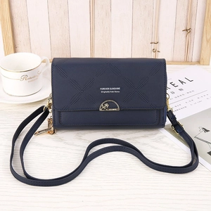 Detail of dark blue embossed leather crossbody bag with gold lock on wooden surface