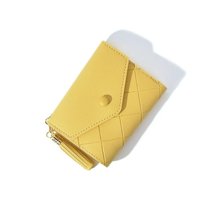 Detail of yellow quilted wallet featuring a tassel charm and triangle metal pendant