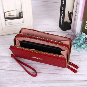 Close-up of a red leather wallet with double zippers and wrist strap on a wooden desk