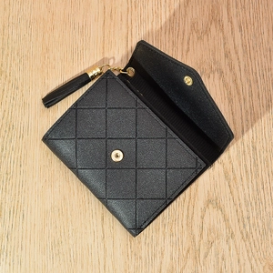 Detail of black quilted leather wallet featuring tassel and golden triangle pendant