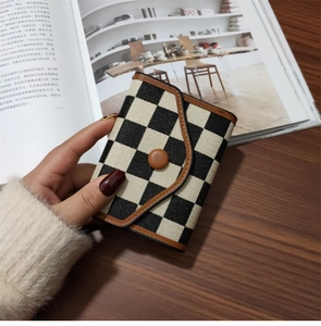 Classic black and white checkered wallet with brown leather trim held over a desk