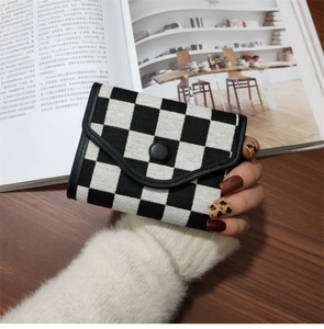 Foldable checkerboard wallet with black leather trim held by hand on wooden desk