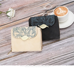 Close-up of beige and black short wallets with leaf prints and gold metal leaf clasps