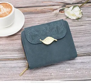 Detail of teal matte leather wallet featuring leaf pattern embossing and gold leaf charm