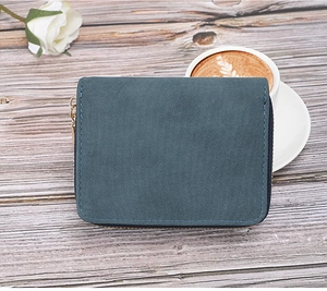 Detail of dark teal short zipper wallet with gold ring pull on grey wood background
