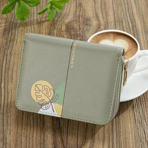 Short mint green zip-around wallet featuring a leaf print and gold hardware on wood