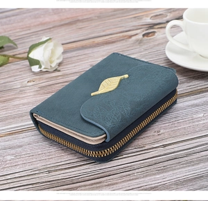 Detailed view of dark green leather wallet with gold leaf buckle and embossed texture
