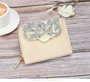 Detail of leaf print beige wallet with gold metal leaf buckle on wooden surface