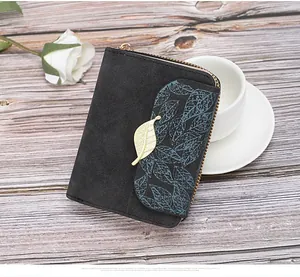 Detail of black matte leather wallet with golden leaf pendant and floral pattern