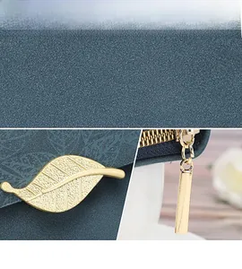 Detail view of the golden leaf clasp and metal zipper on textured blue leather wallet