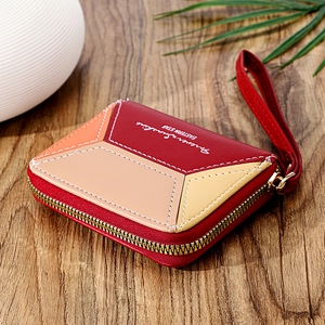 Detail of color-block wallet with zip-around closure and red wrist strap on wooden table