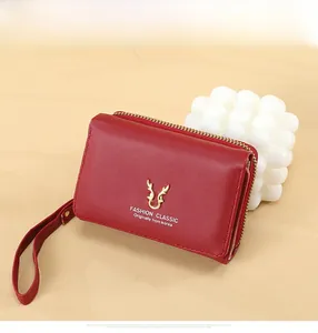 Detail of red PU leather wallet with golden deer head metal logo and wristlet strap
