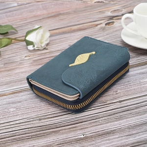 Close-up of deep teal short wallet with golden leaf clasp on a light wood background