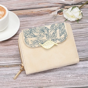 Short printed beige floral wallet for women with golden leaf clasp on a wooden desk