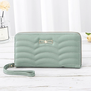 Long mint green women's wallet with wave quilting and golden bow charm on wood surface