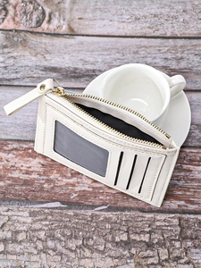 Detail of cream multi-slot card holder with gold zipper on dark wood background