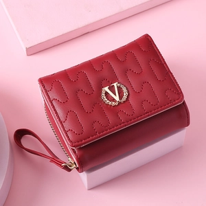 Macro detail of wine red quilted wallet featuring a gold V logo and smooth zipper closure