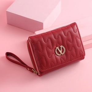 Macro shot of red leather quilted wallet featuring golden metal leaf logo and wrist strap