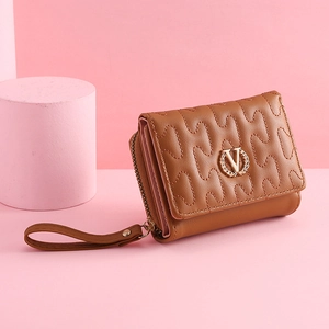 Detail view of brown quilted wallet with golden V-logo and pink lining on creative stage