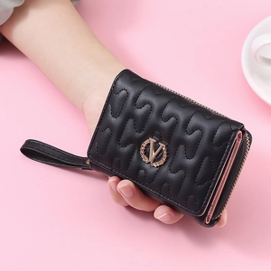 Detail view of black quilted trifold wallet with gold V-badge and pink interior layers