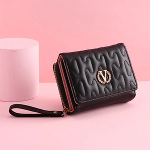 Detail of black quilted tri-fold wallet with golden V logo and wristlet on pink background