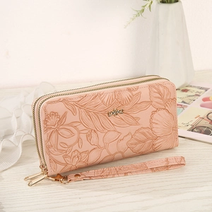 Pink floral embossed long wallet with double zippers and golden bow charm on a table