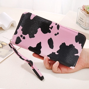Pink and black cow print long zip-around wallet with wristlet strap in hand view