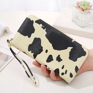 Women's long cow print zipper wallet with wrist strap held by hand in home setting