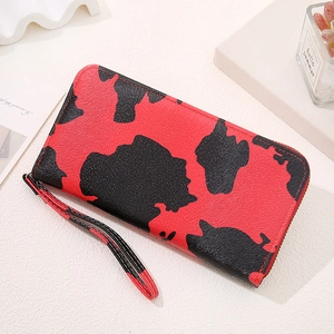 Detail of red and black cow print long wallet with zipper and wristlet strap on flat lay