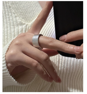 Detail of multi-layered silver ring with vertical textures on a knit sweater background