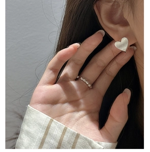 Gros plan d'une boucle d'oreille cœur en argent S925 et d'une bague perlée sur modèle