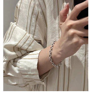 Detail of silver chain bracelet with oval links on wrist against a linen shirt background