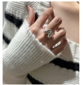 Close-up of minimalist S925 sterling silver heart ring worn on finger with knit background