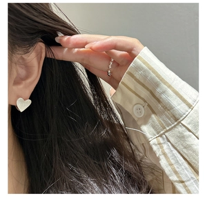 Détail des boucles d'oreilles cœur en argent brossé et bague perlée sur mannequin