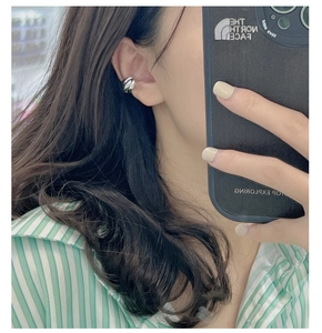 Detail of a three-layer twisted silver ear cuff worn on the ear without piercing
