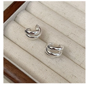 Detailed macro view of triple-layered silver ear cuffs on a cream jewelry box display