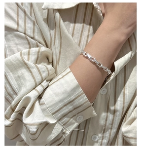 Macro detail of silver paperclip link bracelet on wrist over a striped shirt