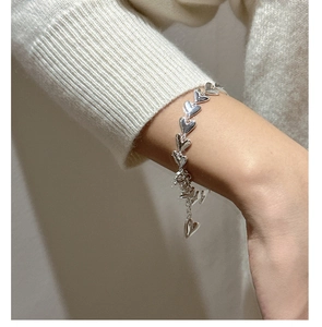 Detailed view of a silver heart-shaped chain bracelet worn on a female wrist over a sweater
