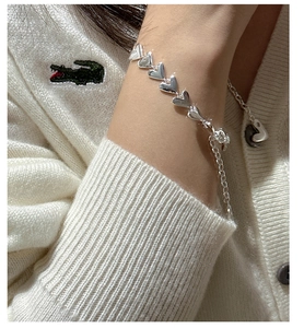 Close-up of S925 sterling silver heart link bracelet worn on wrist with cream knitwear
