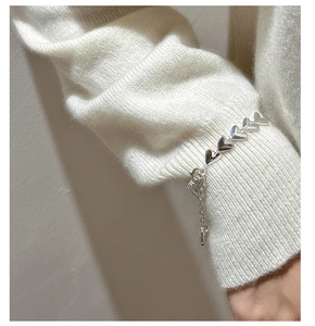 Macro detail of silver heart link bracelet worn over a cozy knitted beige sweater