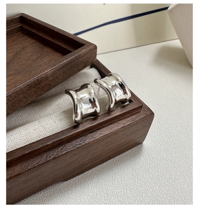 Detailed close-up of polished silver wavy earrings on a premium wooden jewelry box display