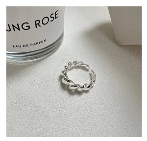 Macro detail of silver twisted croissant ring on textured surface next to perfume