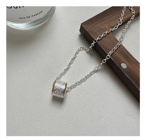 Macro detail of S925 silver cylinder pendant with floral engraving and gold beaded edges