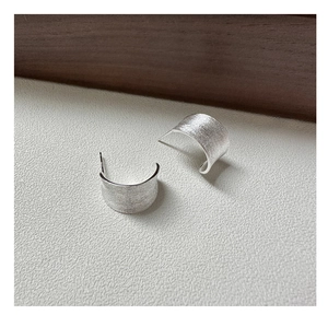 Macro detail of S925 sterling silver curved stud earrings with brushed metallic texture