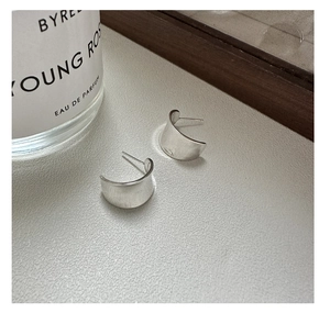 Detailed view of matte silver C-shaped earrings on grey leather texture surface